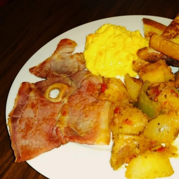 A breakfast plate with ham, scrambled eggs, home fries with peppers and onions, and toast.