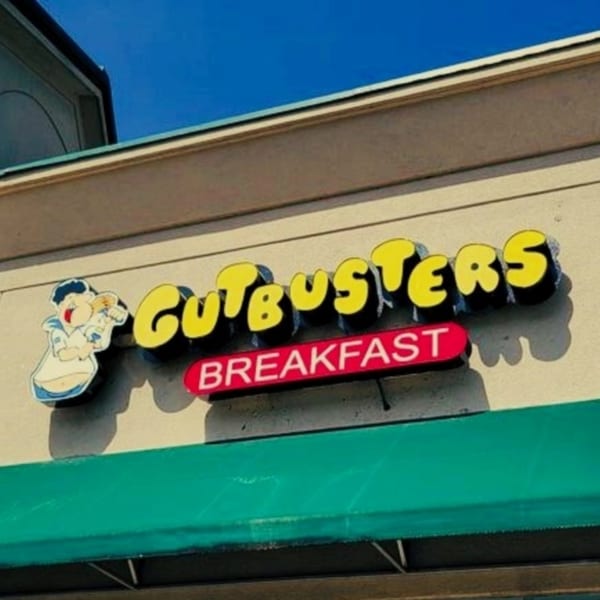 The Gutbusters Breakfast sign features yellow letters, a cartoon chef, and a red "BREAKFAST" banner.