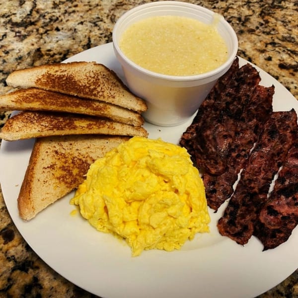 A Gutbusters Breakfast plate with scrambled eggs, crispy bacon, toast, and a side of grits.